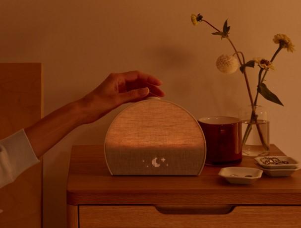 A hand resting on a Hatch Restore clock on a nightstand