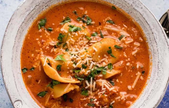 A bowl of creamy tortellini soup with herbs and cheese