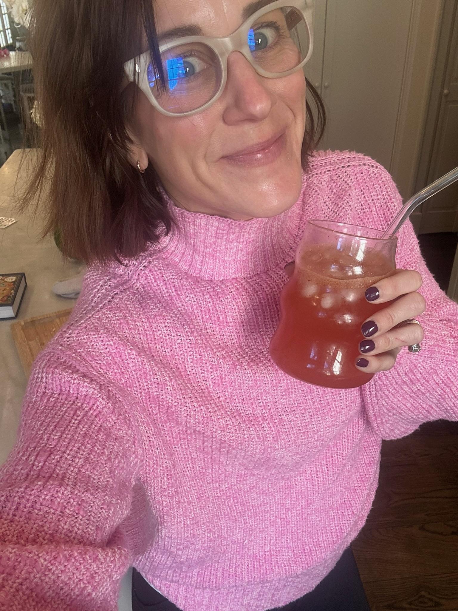 Louise in a pink sweater with a glass of iced hibiscus at the kitchen counter